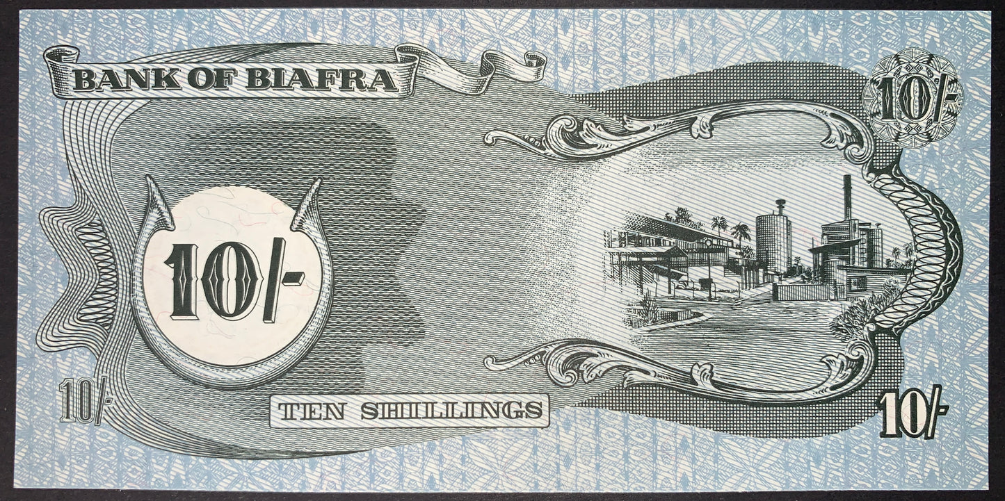 Reverse of the authentic Biafra 10 Shillings banknote ND (1968–1969) P-4 depicting an industrial refinery and factory complex within an ornate engraved frame, with denomination panels and decorative security patterns.