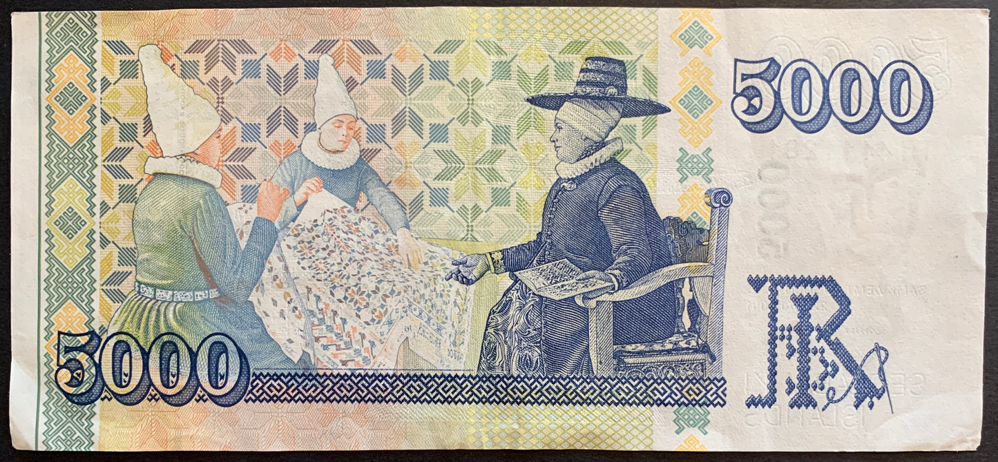Reverse of the Iceland 5000 Krónur 2001 banknote showcasing ornate artwork inspired by traditional 18th-century Icelandic embroidery. Decorative motifs, floral elements, and woven-style patterns fill the composition in rich purple and violet hues. The denomination ‘5000’ is shown clearly, and the overall design highlights Iceland’s cultural and artistic heritage.