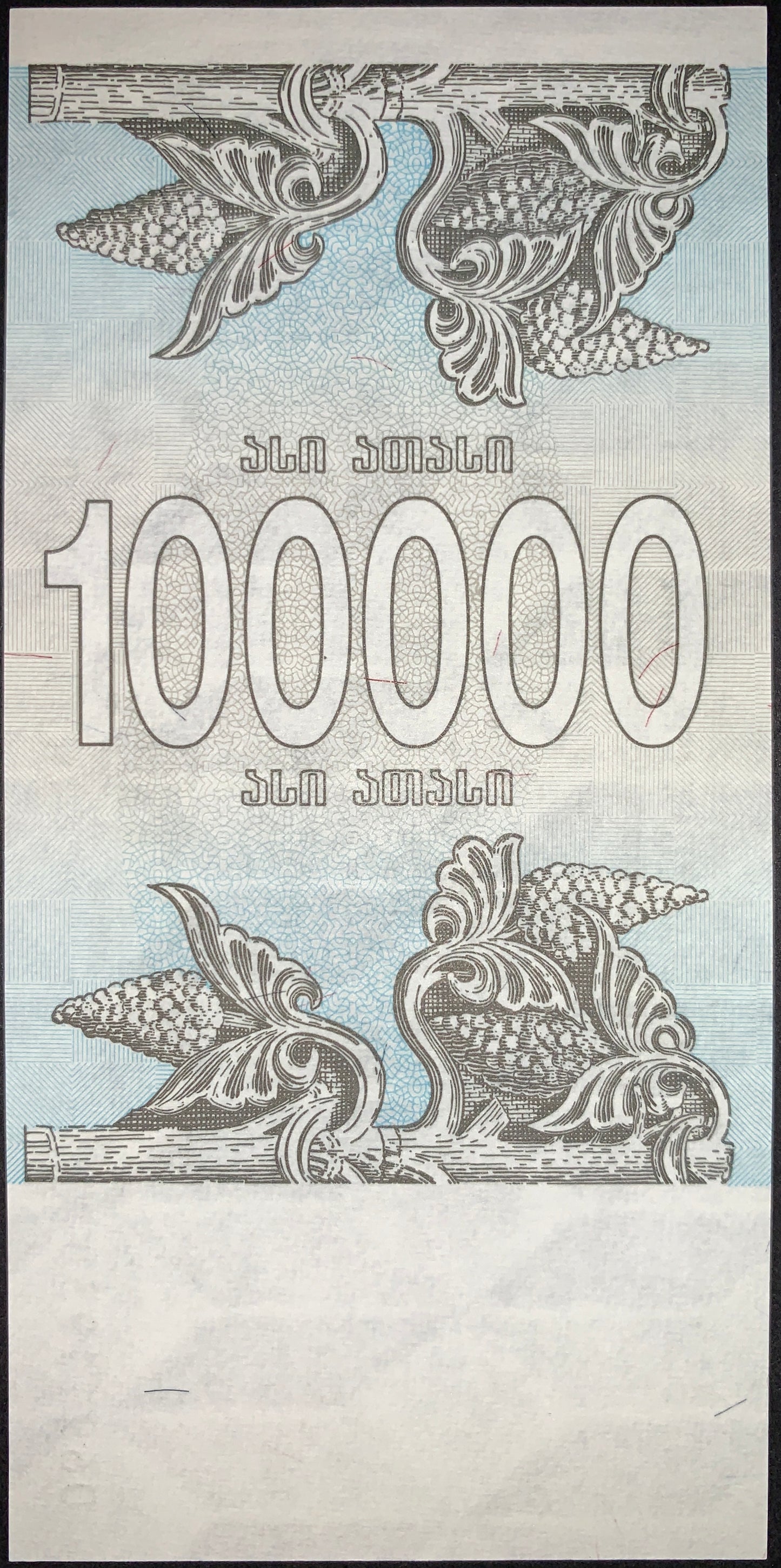 Reverse of the Georgia 100,000 Kuponi note displaying decorative floral and vine motifs surrounding large denomination numerals. Printed in light blue and gray tones with intricate guilloche patterns characteristic of early post-Soviet banknotes.