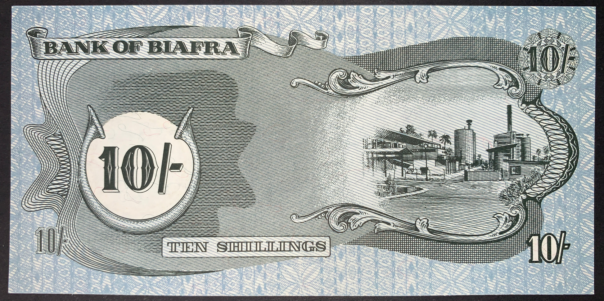 Reverse of the authentic Biafra 10 Shillings banknote ND (1968–1969) P-4 depicting an industrial refinery and factory complex within an ornate engraved frame, with denomination panels and decorative security patterns.