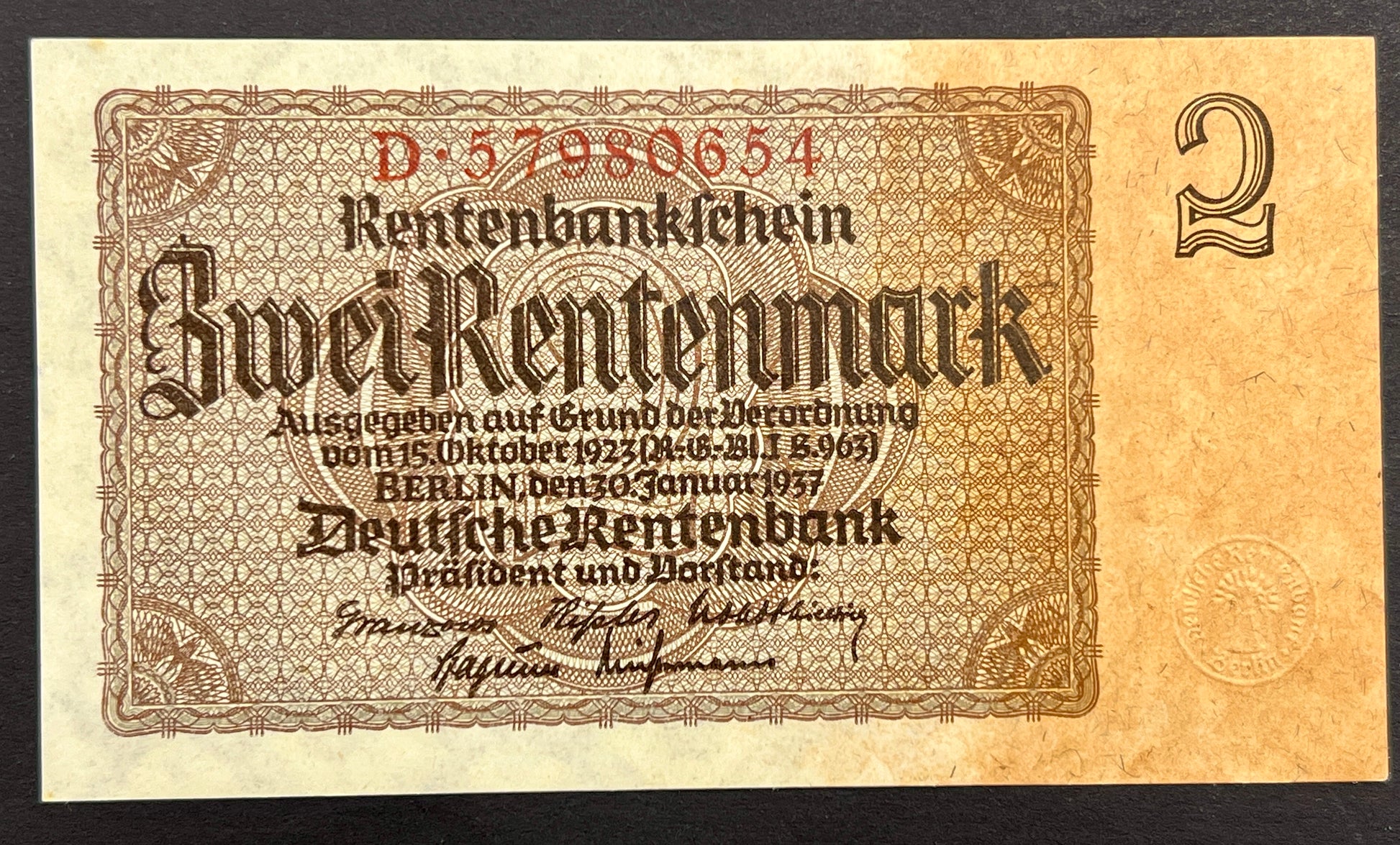 A vintage German Rentenbank 2-mark banknote from 1937, displayed flat against a solid black background. The note features ornate brown and beige security patterns with red serial numbers and black text.