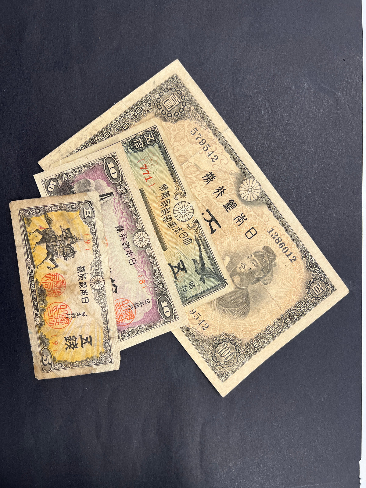 Front view of a vintage Japanese banknote bundle featuring a 1944 100 Yen with Prince Shotoku, and WWII-era 5, 10, and 50 Sen fractional notes with historic shrines and statues.