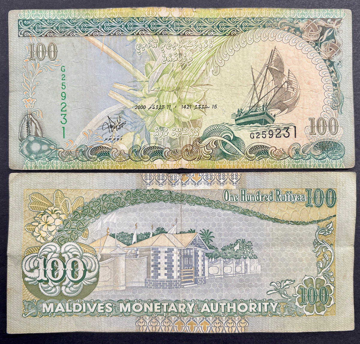 Front view of a circulated 2000 Maldives 100 Rufiyaa banknote featuring a traditional Dhoni sailing boat, a coconut palm, and a cowrie shell. Back view of a vintage 2000 Maldives 100 Rufiyaa banknote showcasing a detailed engraving of the historic Medhu Ziyaaraiy shrine in Male.
