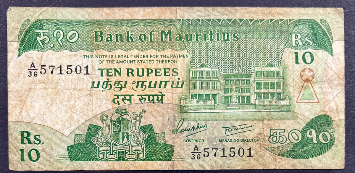Front view of a circulated 1985 Mauritius 10 Rupees banknote featuring the national coat of arms and the historic Government House building in Port Louis.
