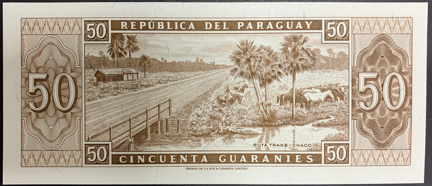 Reverse of a Paraguay 50 Guaraníes banknote (P-197b) featuring an engraved rural landscape of the Trans-Chaco Route in Paraguay. The scene includes a wooden bridge crossing a waterway, palm trees, open countryside, cattle grazing near the water, and a small structure in the distance. Large denomination numerals appear on both sides, surrounded by detailed ornamental patterns and fine-line engraving. Actual serial numbers may vary as multiple banknotes are available.