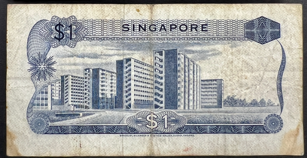 Back view of a vintage 1967 Singapore 1 Dollar banknote showcasing a detailed engraving of modern high-rise public housing apartments.
