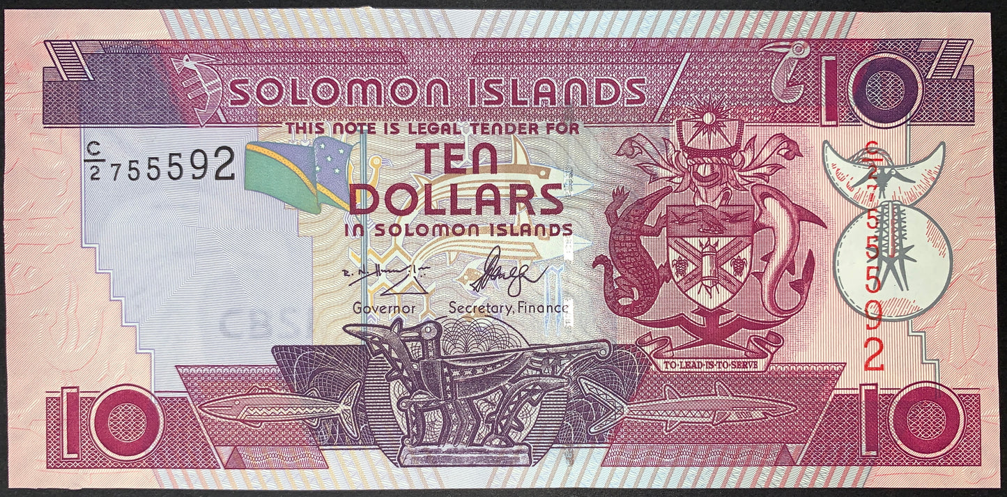 Obverse view of a pink and plum-purple Solomon Islands 10-dollar banknote in crisp uncirculated condition. The design features a large, billowing national flag in the center and the official national Coat of Arms on the right side. It displays the signatures of Governor Rick N. Houenipwela and Secretary of Finance Shadrach Fanega in the center. The horizontal serial number C/2 755592 is printed in black ink on the upper-left, and a vertical serial number is printed in red ink on the right. Intricate geometr