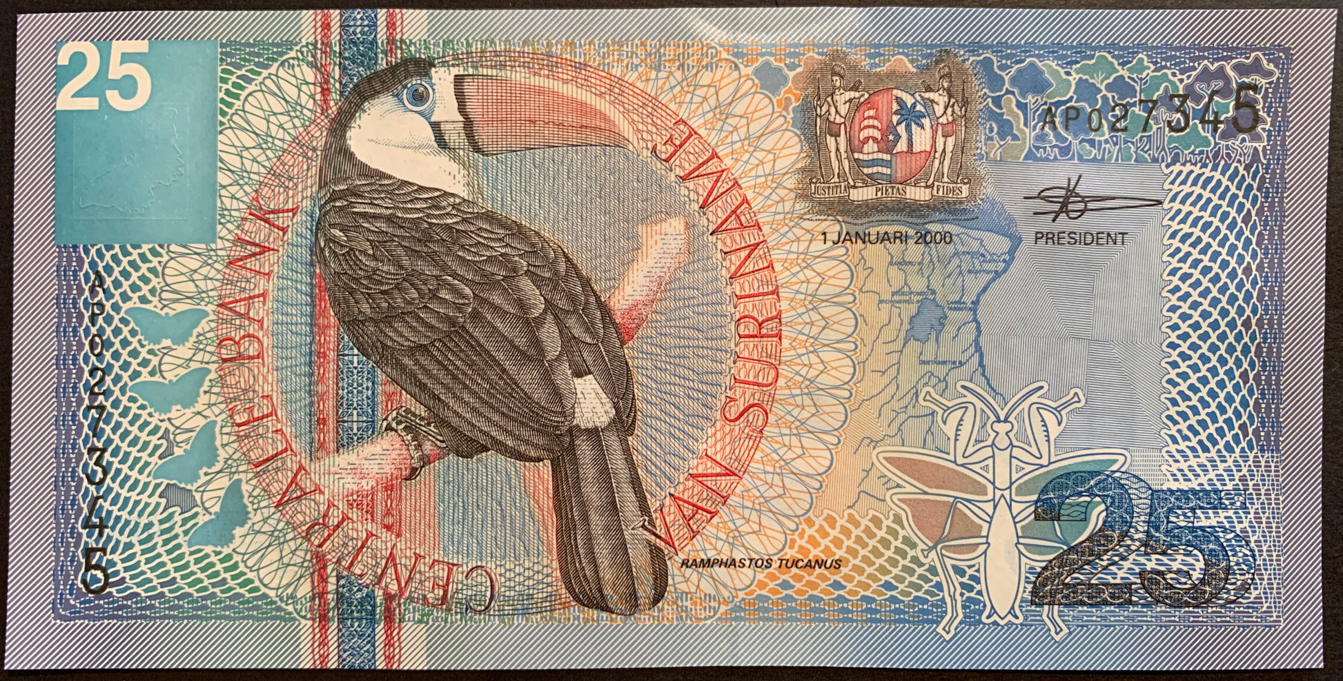 front of Suriname 25 Gulden 2000 P-148 collectible banknote with Red-billed White-throated Toucan (ramphastos tucanus); Butterflies and a Leaf-mimicking praying mantis