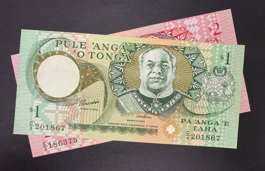 Obverse view of a Tonga uncirculated banknote bundle showing the green 1 Pa'anga note stacked on top of a pink 2 Pa'anga note. The 1 Pa'anga note prominently features a detailed portrait of King Tāufaʻāhau Tupou IV in the center, with the national Coat of Arms on the right side and a circular watermark window on the left. The text "PULE 'ANGA O TONGA" is printed at the top left. The black serial number C/4 201867 is printed horizontally on both the lower-left and lower-right corners.