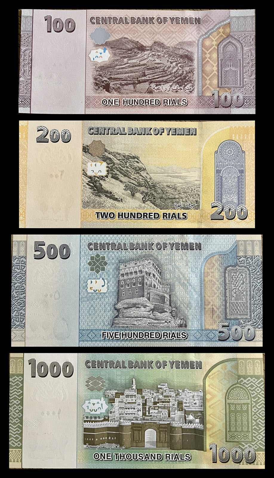 Back view of a Yemen 100, 200, 500 and 1000 Rials set showing mountain terraces, the Hawf landscape of Al-Mahra, Dar al-Hajar Rock Palace and Bab al-Yemen in Old Sana’a.