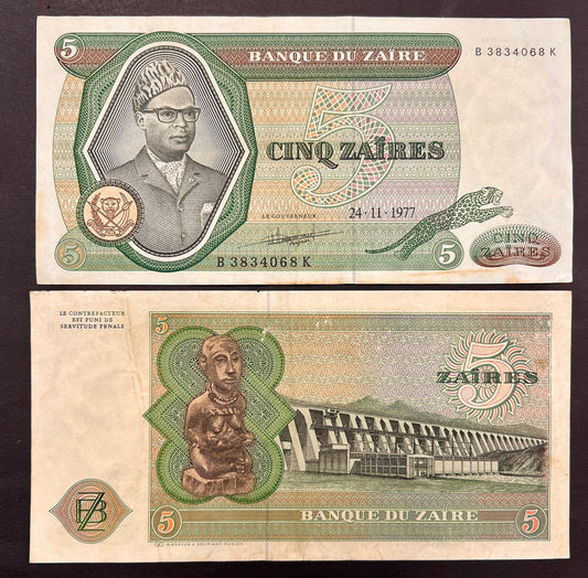 Front view of a circulated 1977 Zaire 5 Zaires banknote featuring a portrait of President Mobutu Sese Seko wearing his signature leopard-print hat, alongside a leaping leopard. Back view of a vintage 1977 Zaire 5 Zaires banknote showcasing a traditional carved wooden statue and an engraving of the massive Inga Dam.
