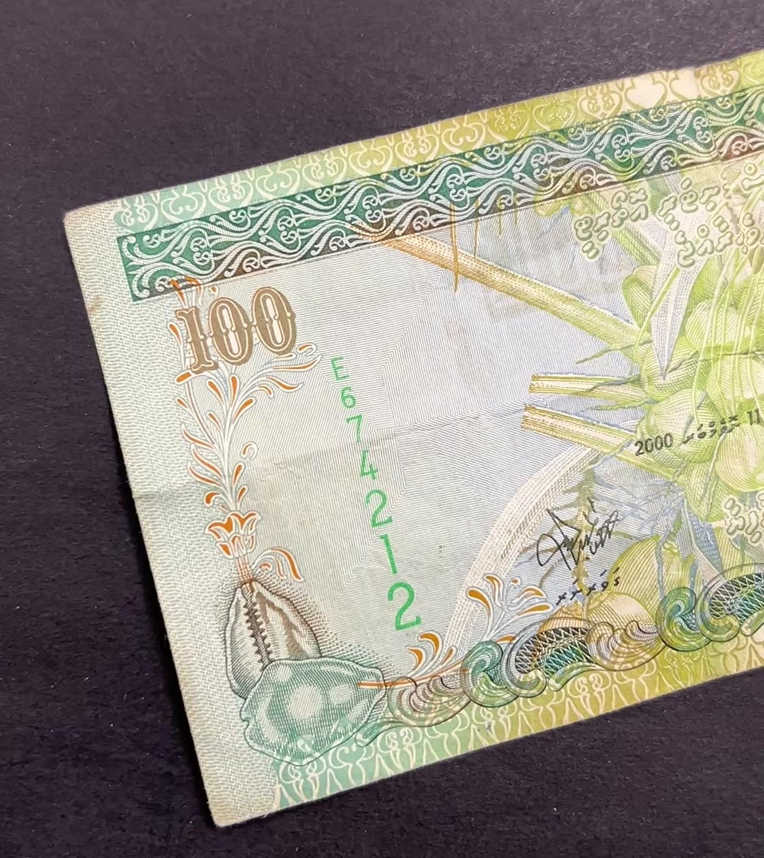 Front view of a circulated 2000 Maldives 100 Rufiyaa banknote featuring a traditional Dhoni sailing boat, a coconut palm, and a cowrie shell.
