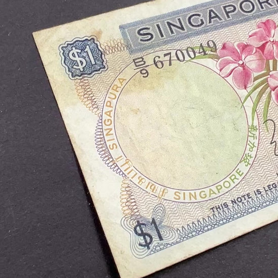 Front view of a circulated 1967 Singapore 1 Dollar banknote featuring a beautiful pink Vanda Joaquim orchid and the Singaporean national coat of arms.