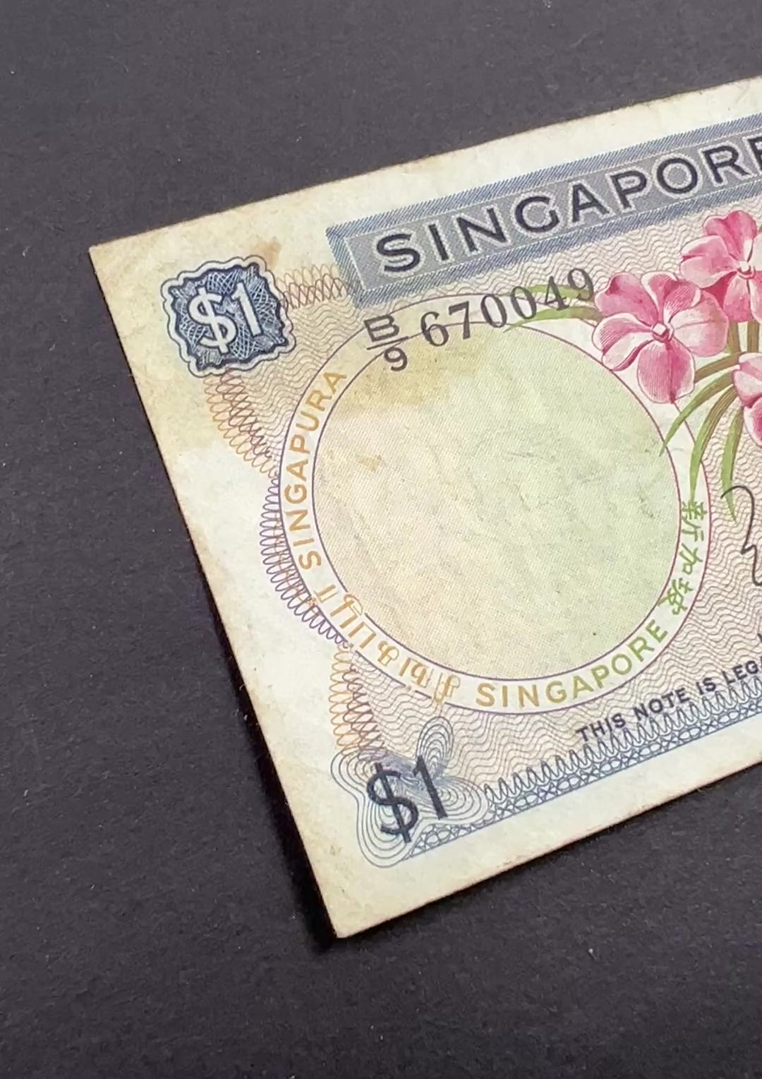 Front view of a circulated 1967 Singapore 1 Dollar banknote featuring a beautiful pink Vanda Joaquim orchid and the Singaporean national coat of arms.