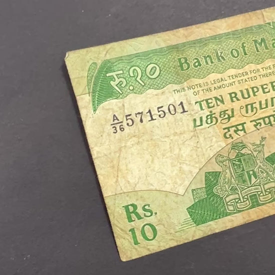 Front view of a circulated 1985 Mauritius 10 Rupees banknote featuring the national coat of arms and the historic Government House building in Port Louis.
